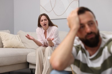 Photo of Betrayal. Angry woman shouting at her offended husband on sofa at home, selective focus
