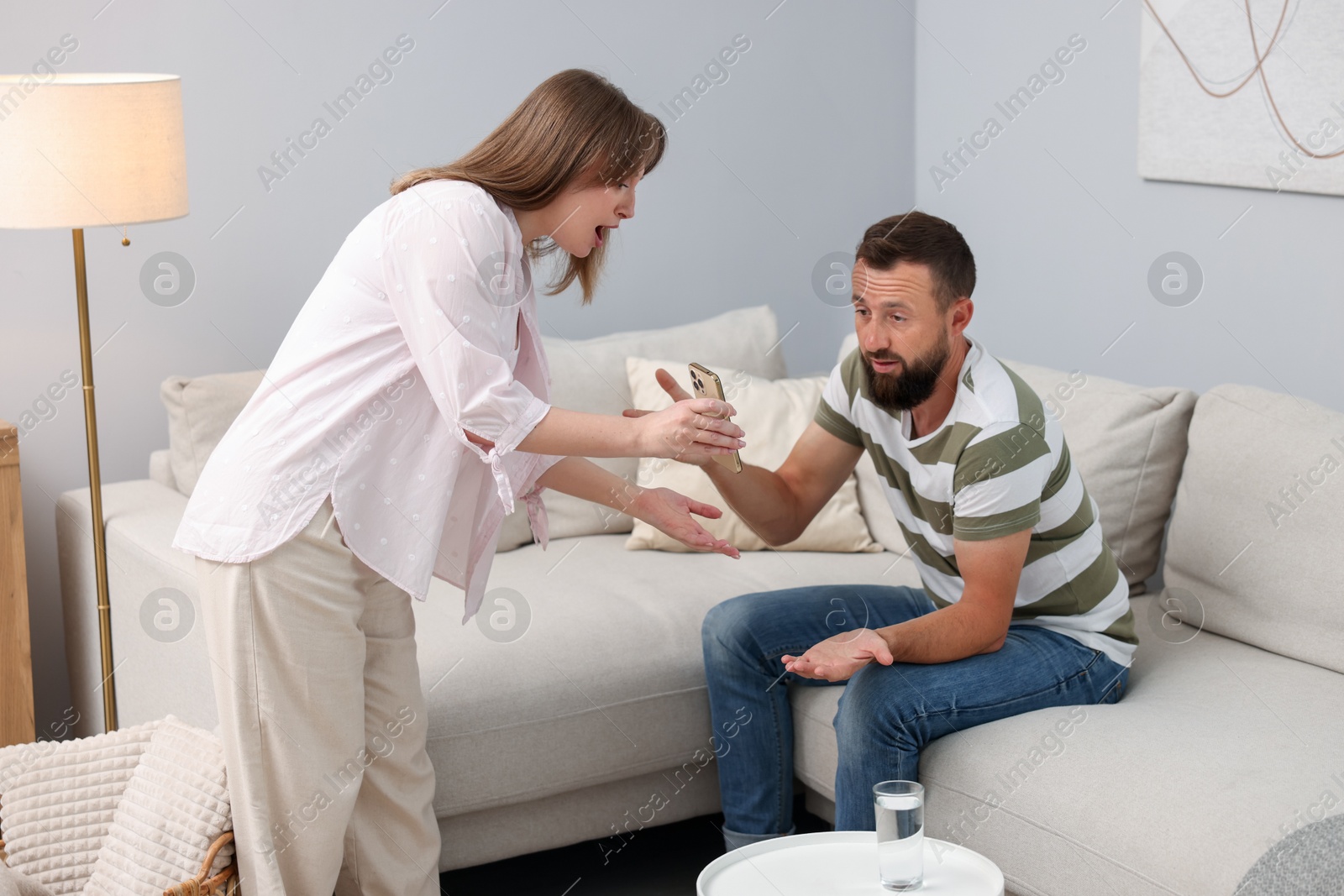 Betrayal. Wife showing smartphone with proofs to her unfaithful husband at home Photo of Betrayal. Wife showing smartphone with proofs to her unfaithful husband at home