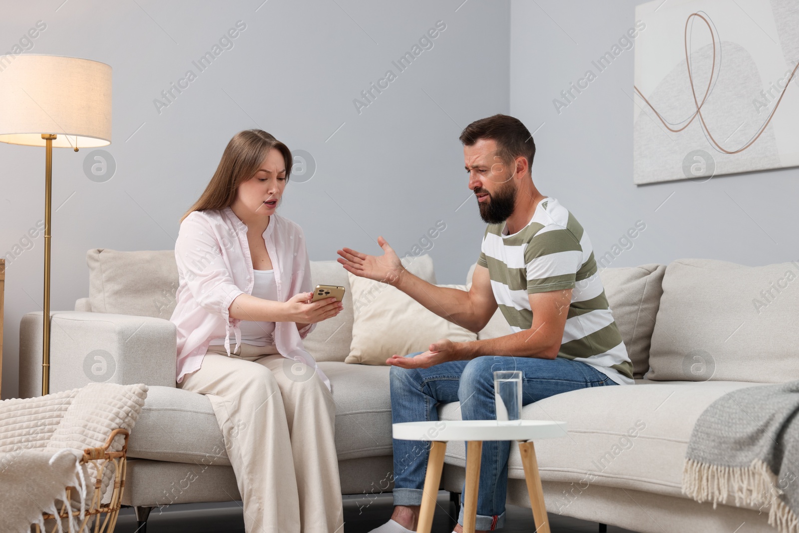 Betrayal. Wife showing smartphone with proofs to her unfaithful husband on sofa at home Photo of Betrayal. Wife showing smartphone with proofs to her unfaithful husband on sofa at home