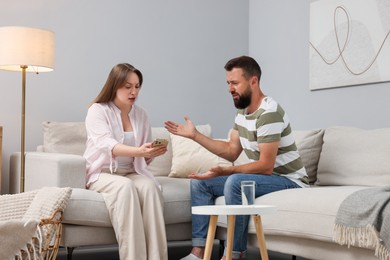 Photo of Betrayal. Wife showing smartphone with proofs to her unfaithful husband on sofa at home