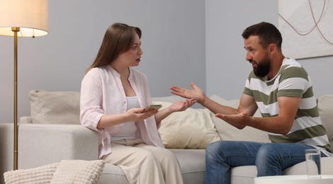 Photo of Betrayal. Wife showing smartphone with proofs to her unfaithful husband on sofa at home