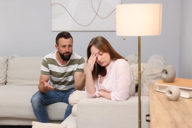 Photo of Betrayal. Man talking to his frustrated wife on sofa at home