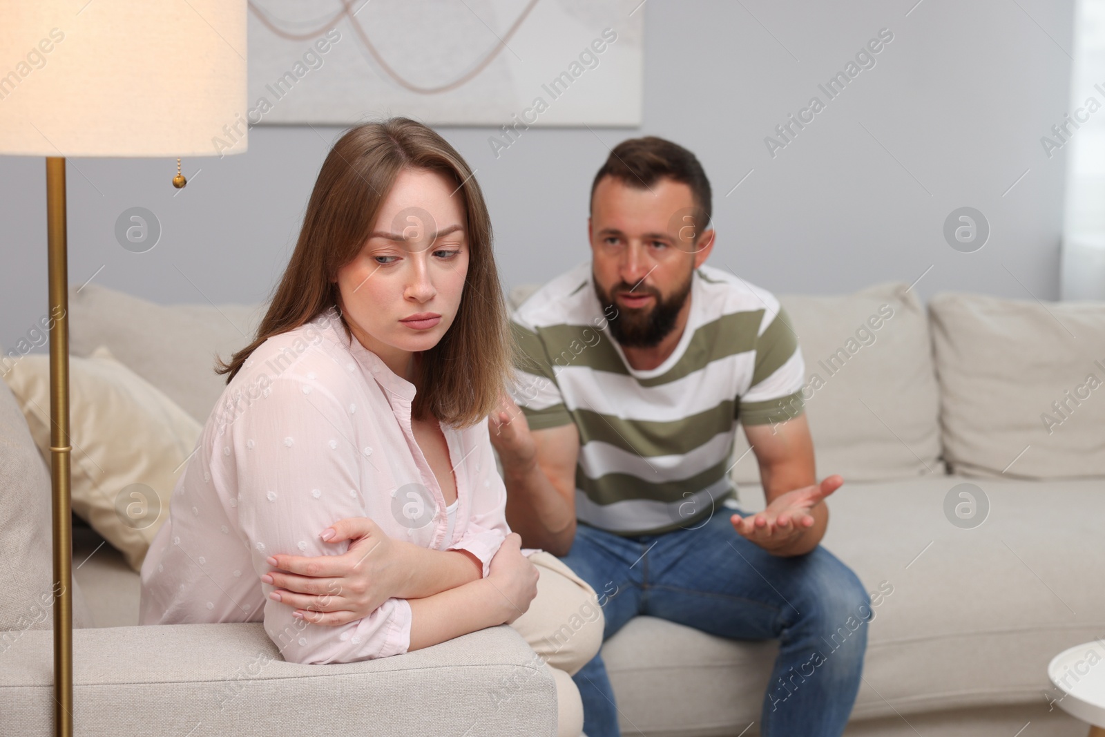 Photo of Betrayal. Man talking to his frustrated wife on sofa at home