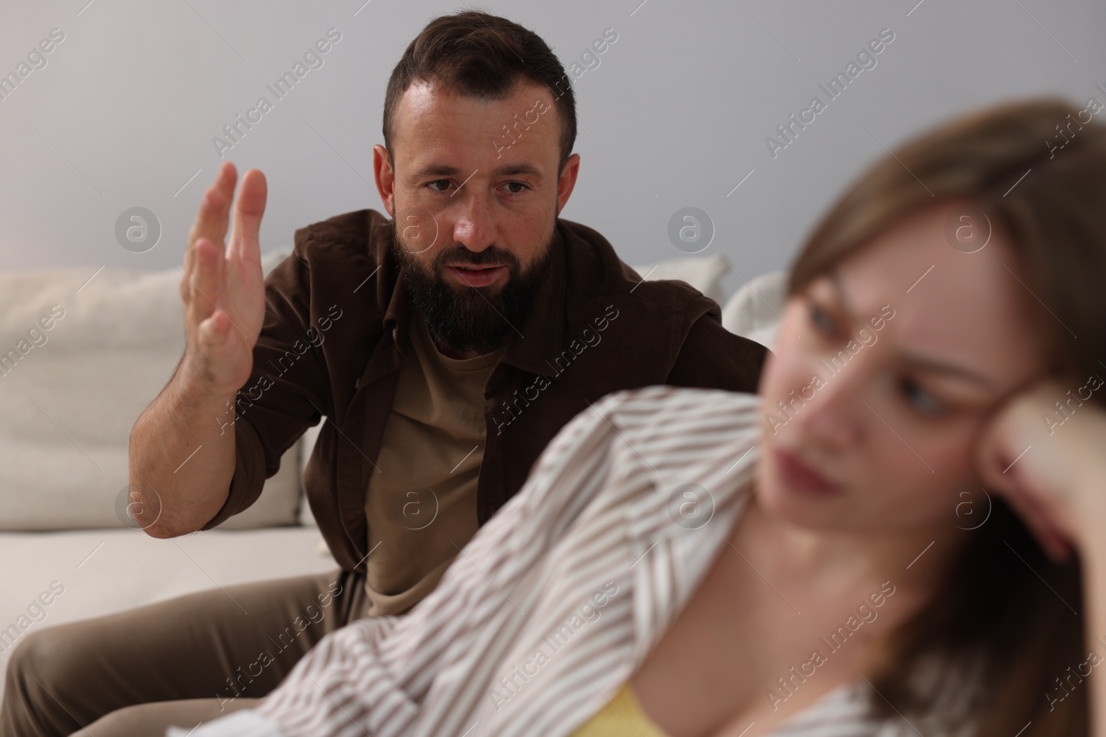 Betrayal. Man talking to his offended wife on sofa at home, selective focus Photo of Betrayal. Man talking to his offended wife on sofa at home, selective focus