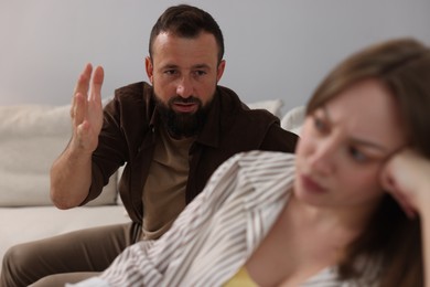 Photo of Betrayal. Man talking to his offended wife on sofa at home, selective focus