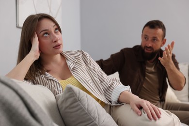 Photo of Betrayal. Man talking to his offended wife on sofa at home, selective focus