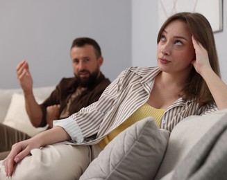 Photo of Betrayal. Man talking to his offended wife on sofa at home, selective focus