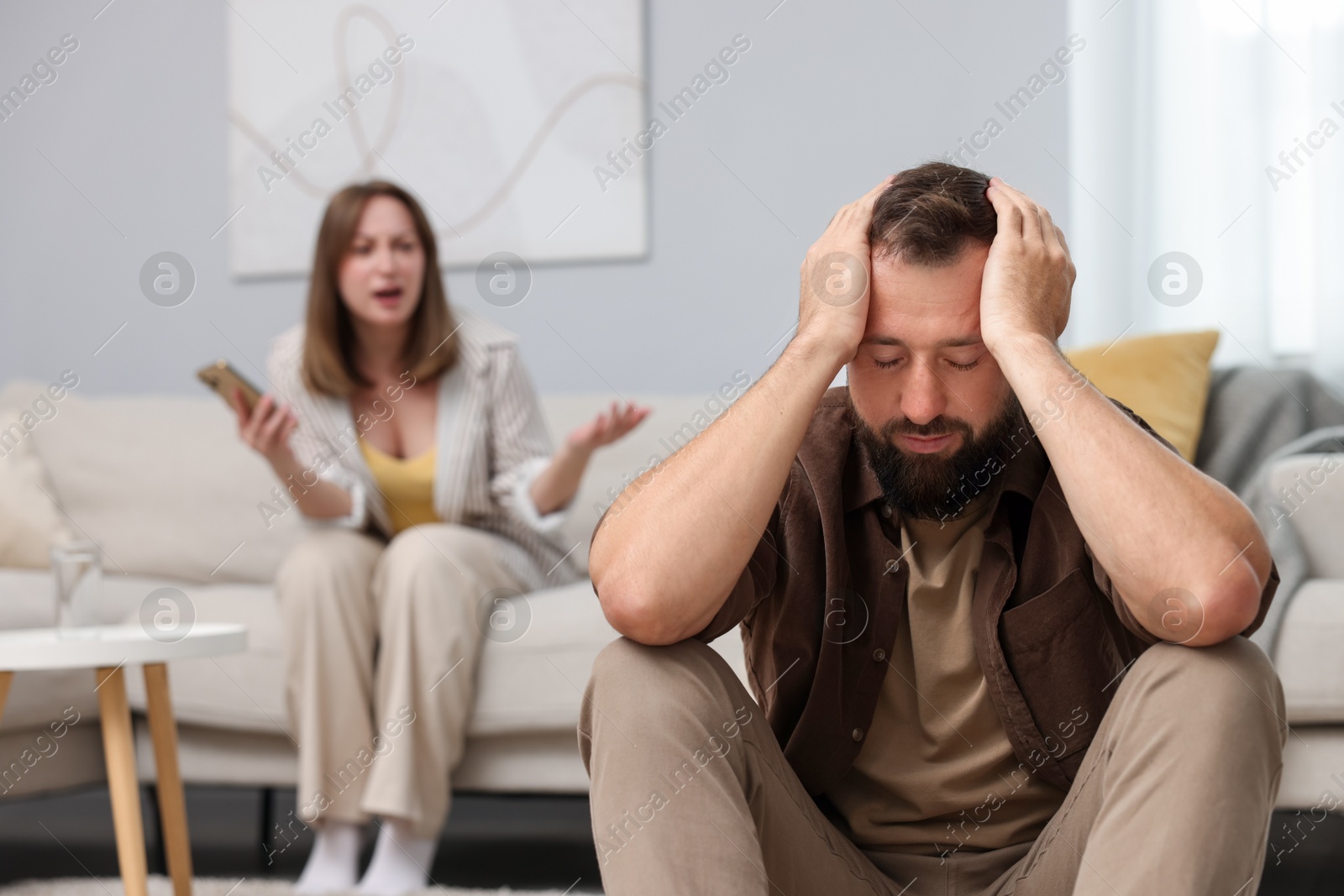 Betrayal. Angry woman with smartphone shouting at her offended husband on sofa at home, selective focus Photo of Betrayal. Angry woman with smartphone shouting at her offended husband on sofa at home, selective focus