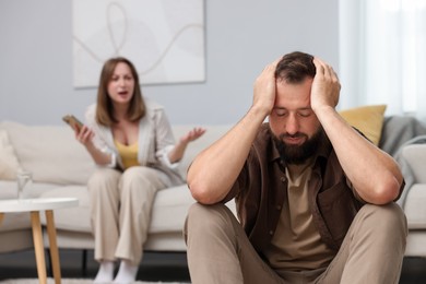 Photo of Betrayal. Angry woman with smartphone shouting at her offended husband on sofa at home, selective focus