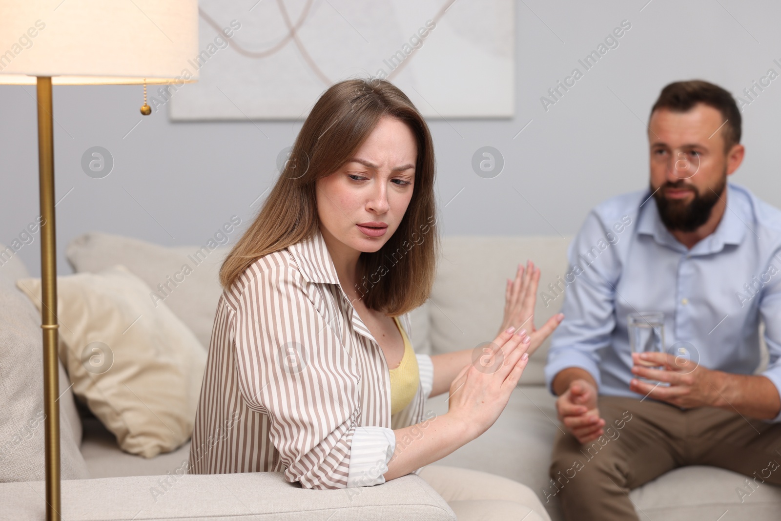 Photo of Betrayal. Husband apologizing to his offended wife while she stopping him on sofa at home, selective focus