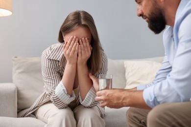 Photo of Betrayal. Husband with glass of water apologizing to his offended wife on sofa at home