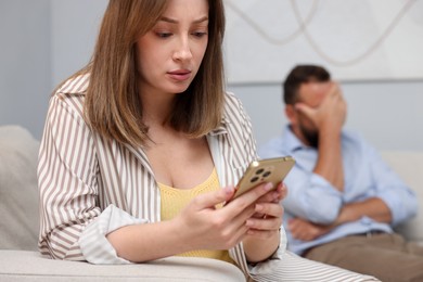 Photo of Betrayal. Jealous woman finding proofs of her unfaithful husband on smartphone on sofa at home, selective focus