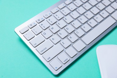 Photo of Modern wireless computer keyboard and mouse on turquoise background, closeup