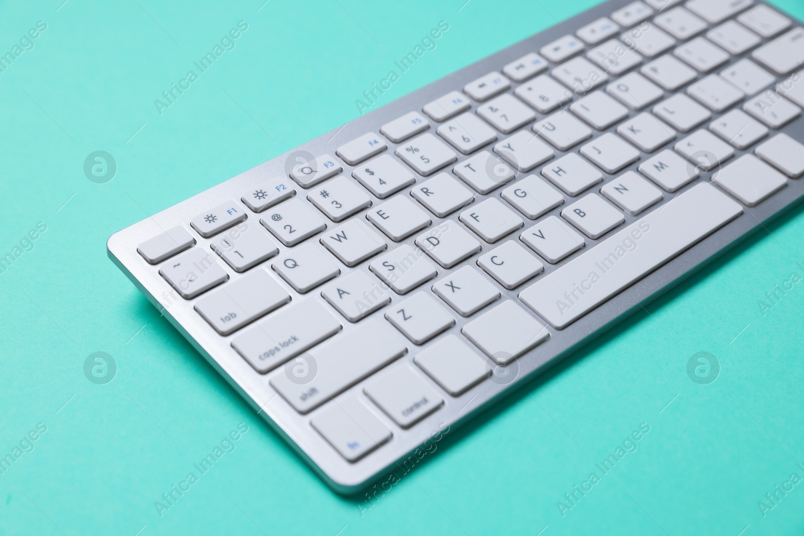 Photo of Modern wireless computer keyboard on turquoise background, closeup