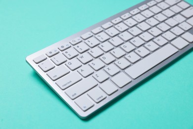 Photo of Modern wireless computer keyboard on turquoise background, closeup