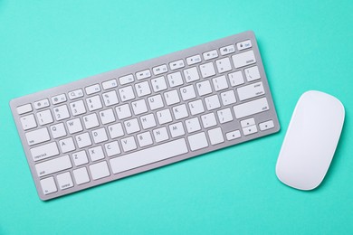 Photo of Modern wireless computer keyboard and mouse on turquoise background, flat lay