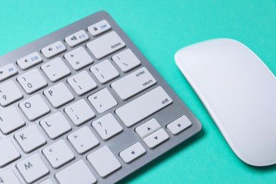 Photo of Modern wireless computer keyboard and mouse on turquoise background, closeup