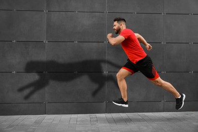 Image of Athletic young man running. His shadow in form of cheetah on wall. Sports poster