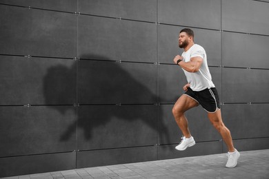 Image of Athletic young man running near wall with his shadow in form of ox. Sports poster