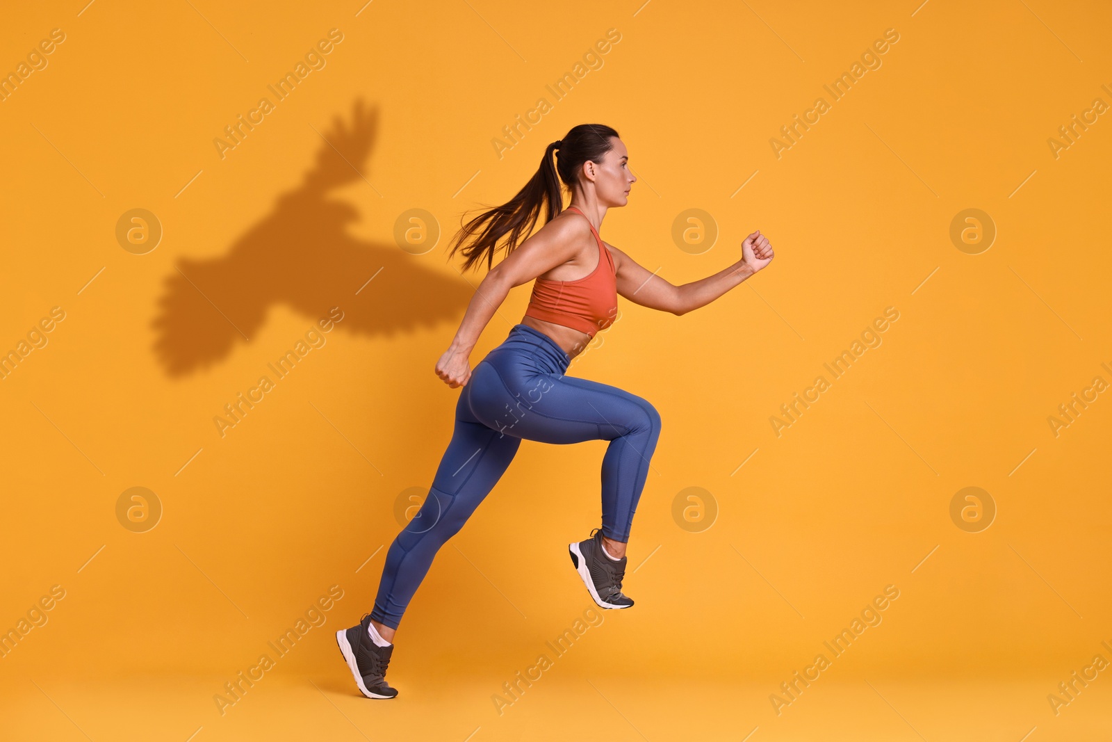 Athletic young woman running against orange background with her shadow in form of hawk. Sports poster Image of Athletic young woman running against orange background with her shadow in form of hawk. Sports poster