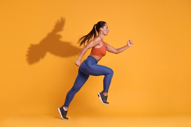 Image of Athletic young woman running against orange background with her shadow in form of hawk. Sports poster