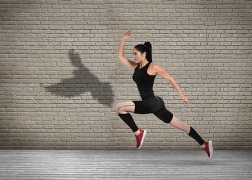 Image of Athletic young woman running. Her shadow in form of hawk on brick wall. Sports poster