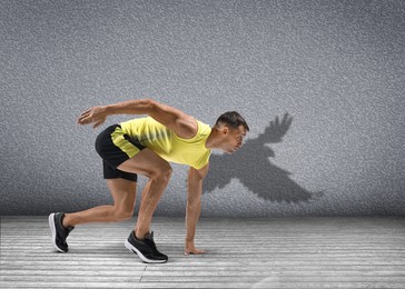 Image of Athletic man on starting position for run. His shadow in form of hawk on grey wall. Sports poster