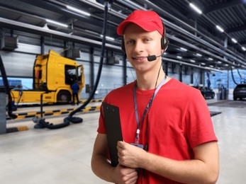 Image of Car service worker with headset and clipboard against truck at station. Client support