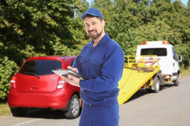 Image of Car service worker with clipboard near red auto and tow truck outdoors