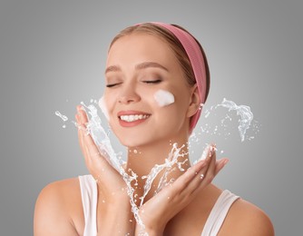 Image of Young woman washing face with cleansing foam and water splash against grey background