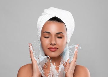 Image of Young woman washing face with cleansing foam and water splash against grey background