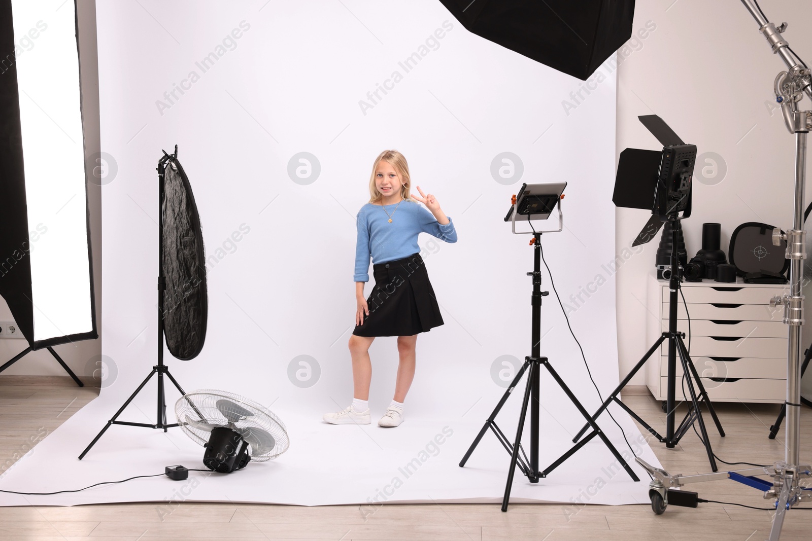 Photo of Little girl showing peace sign on white background in photo studio with professional equipment
