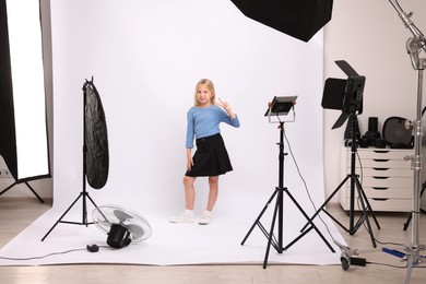Photo of Little girl showing peace sign on white background in photo studio with professional equipment