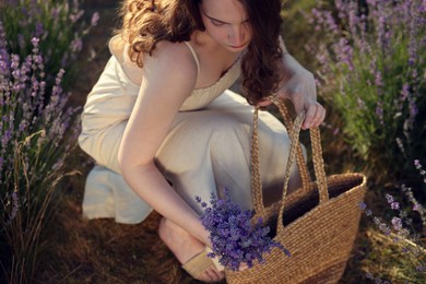 Photo of Beautiful young woman with lavender flowers and wicker bag in field, above view