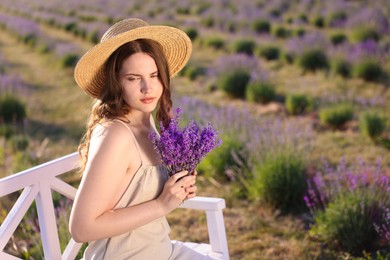 Photo of Beautiful young woman with lavender flowers on bench in field. Space for text