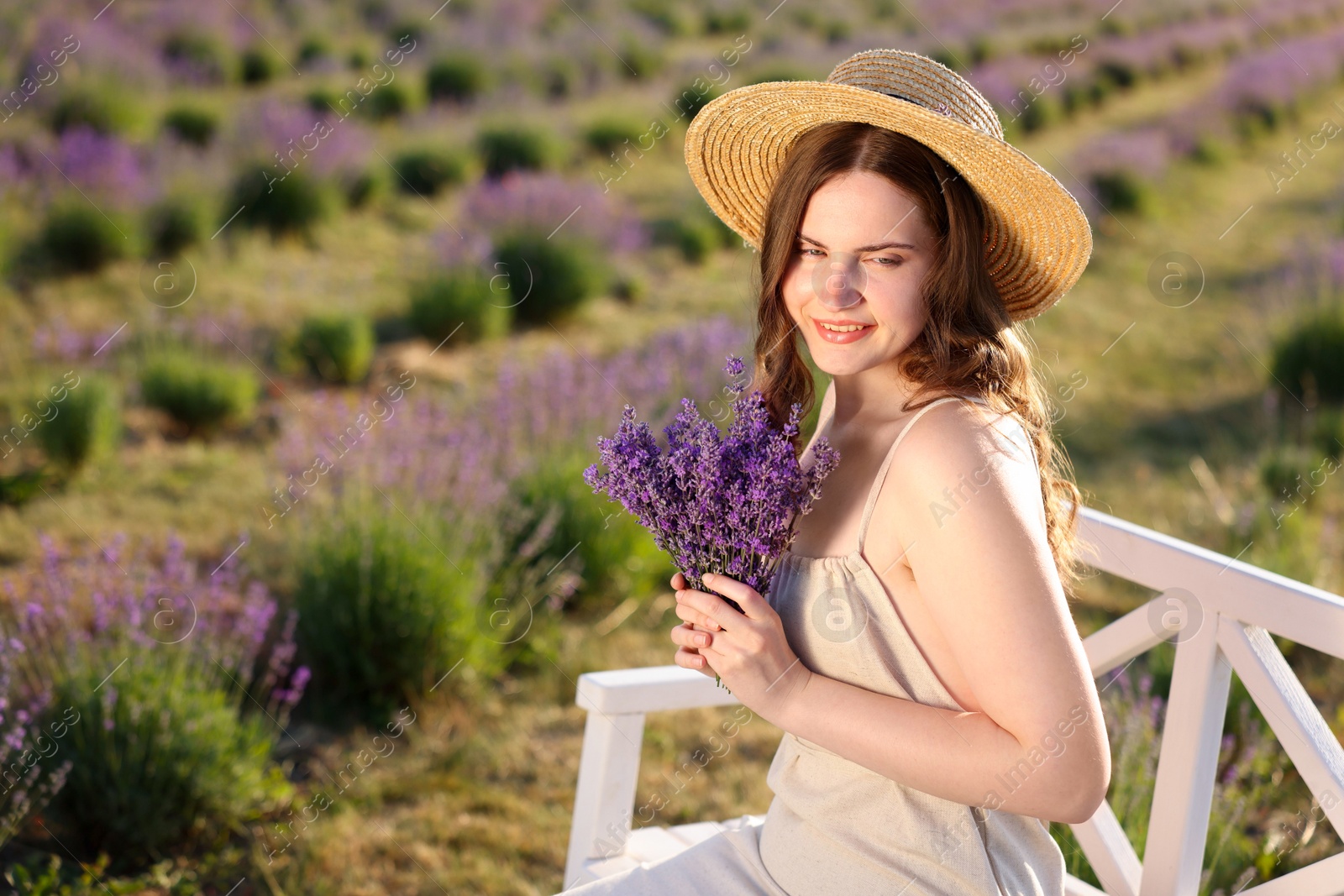 Beautiful young woman with lavender flowers on bench in field. Space for text Photo of Beautiful young woman with lavender flowers on bench in field. Space for text