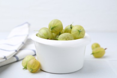 Photo of Fresh green gooseberries in bowl on white table, closeup