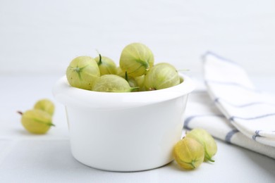Photo of Fresh green gooseberries in bowl on white table, closeup