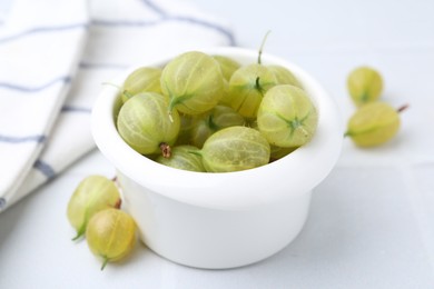 Photo of Fresh green gooseberries in bowl on white table, closeup