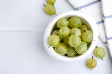 Photo of Fresh green gooseberries in bowl on white table, top view. Space for text
