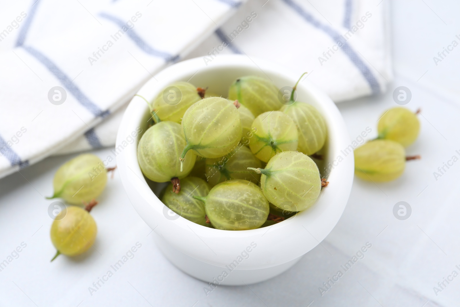 Fresh green gooseberries in bowl on white table, closeup Photo of Fresh green gooseberries in bowl on white table, closeup