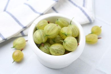 Photo of Fresh green gooseberries in bowl on white table, closeup