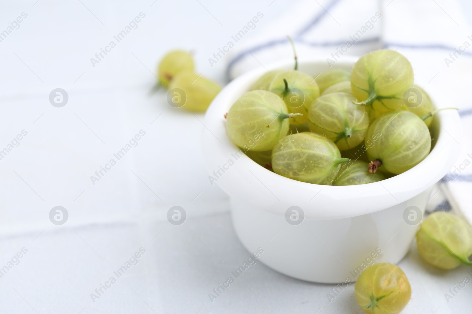 Fresh green gooseberries in bowl on white table, closeup. Space for text Photo of Fresh green gooseberries in bowl on white table, closeup. Space for text