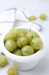 Photo of Fresh green gooseberries in bowl on white table, closeup
