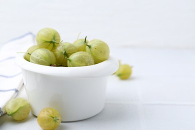 Photo of Fresh green gooseberries in bowl on white table, closeup. Space for text