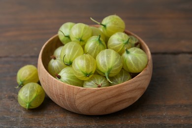 Photo of Fresh green gooseberries in bowl on wooden table, closeup