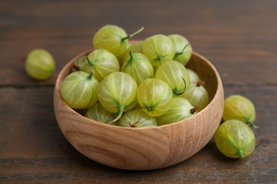 Photo of Fresh green gooseberries in bowl on wooden table, closeup