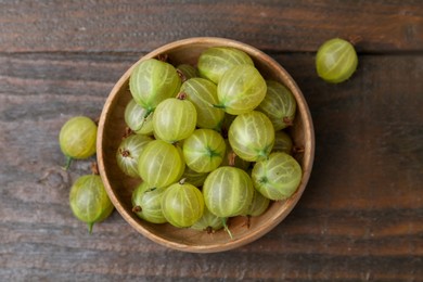 Photo of Fresh green gooseberries in bowl on wooden table, top view
