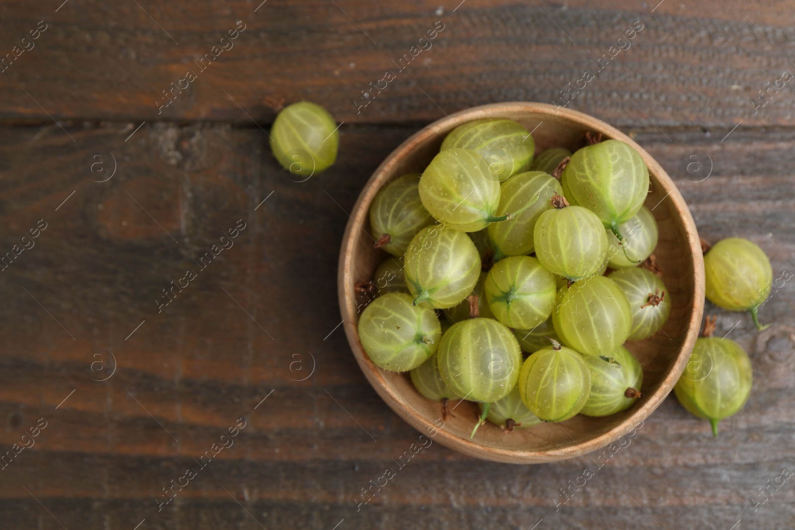 Fresh green gooseberries in bowl on wooden table, top view. Space for text Photo of Fresh green gooseberries in bowl on wooden table, top view. Space for text
