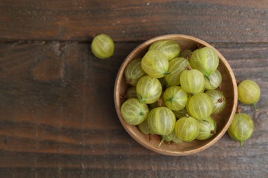 Photo of Fresh green gooseberries in bowl on wooden table, top view. Space for text
